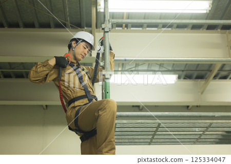 A male worker wearing a full harness climbing scaffolding 125334047