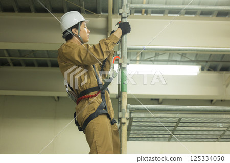 一名身穿全套安全帶的男工人攀爬鷹架 125334050