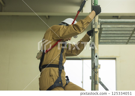 一名身穿全套安全帶的男工人攀爬鷹架 125334051