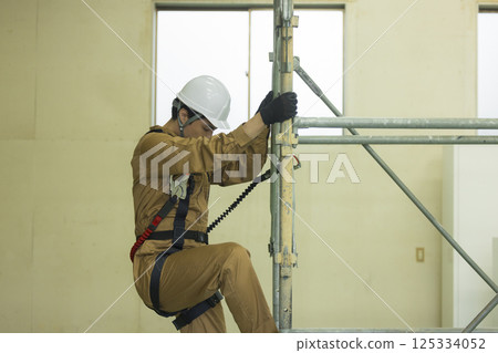 一名身穿全套安全帶的男工人攀爬鷹架 125334052