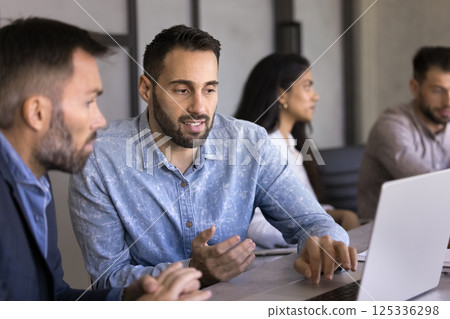 Two colleagues sit at desk working together using laptop Two colleagues sit at desk working together using laptop 125336298