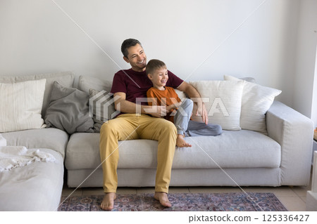 Happy single dad relaxing on sofa hugging smiling little son 125336427