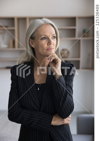 Serious senior age businesswoman stand in office lost in thoughts Serious senior age businesswoman stand in office lost in thoughts 125336489