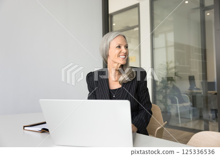 Smiling mature businesswoman visualize success sitting by notebook at workplace 125336536