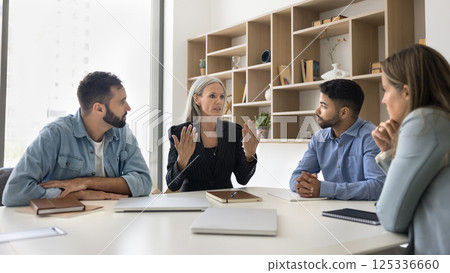 Senior female leader speak to younger team at boardroom desk 125336660