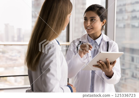 Woman doctor talk to colleague discuss article on tablet screen 125336723