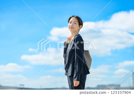 A woman in a suit standing against a blue sky 125337904