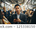 一位商人乘坐擁擠的火車，看著他的智慧型手機 125338150