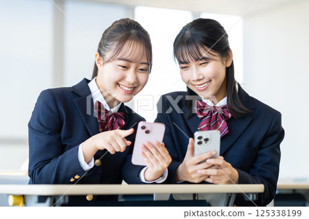 High school girls looking at their smartphones in the classroom. Photo courtesy of Denpa Gakuen, Tokyo Electronics College. 125338199