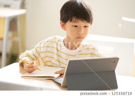 Male elementary school student studying online while looking at a tablet 125338719