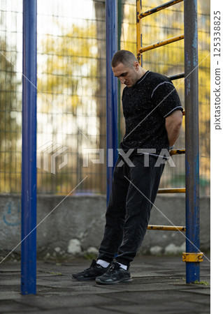 man dressed in black athletic clothing performs workout outdoor gym in city park. setting has serene atmosphere trees in background during daylight. man dressed in black athletic clothing performs workout outdoor gym in city park. setting has serene atmosphere trees in background during daylight. 125338825