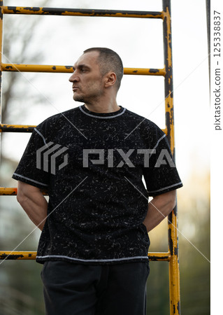 man stands outdoors his hands behind his back posing confidently next yellow ladder. background features soft sunset light illuminating scene. 125338837