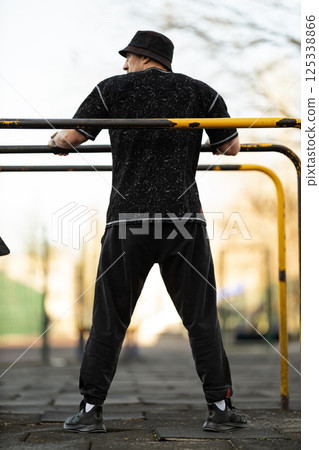 man is engaging in fitness activity outdoor park. He is using workout equipment while dressed casually surrounded natural setting trees. 125338866