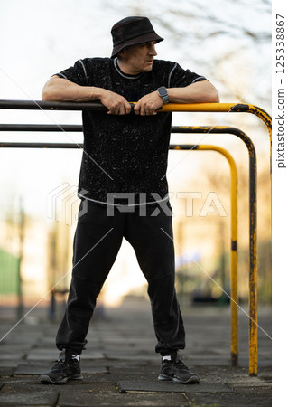 man is actively using outdoor fitness equipment wearing casual athletic clothing. He stands confidently and focuses on his workout routine in city park during early morning light. 125338867