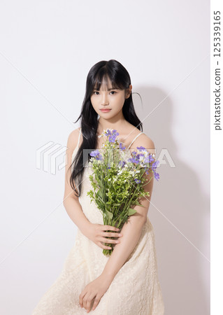 Cropped view of young woman sitting in white dress holding bouquet of purple flowers Cropped view of young woman sitting in white dress holding bouquet of purple flowers 125339165