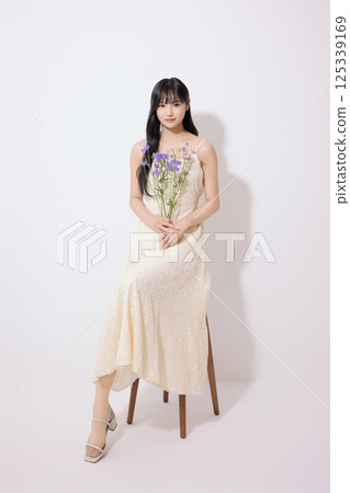 Cropped view of young woman sitting in white dress holding bouquet of purple flowers 125339169