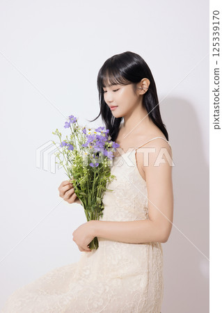 Cropped view of young woman sitting in white dress holding bouquet of purple flowers 125339170