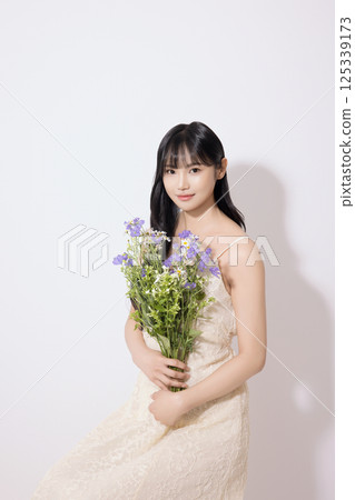 Cropped view of young woman sitting in white dress holding bouquet of purple flowers 125339173