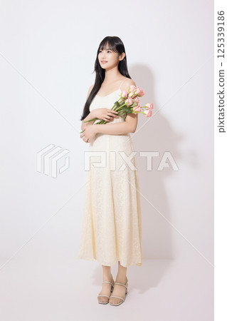 Cropped view of young woman wearing white dress and holding tulips Cropped view of young woman wearing white dress and holding tulips 125339186
