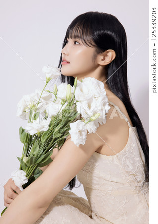 Portrait of a young woman sitting wearing a white dress and holding a bouquet of white flowers Portrait of a young woman sitting wearing a white dress and holding a bouquet of white flowers 125339203