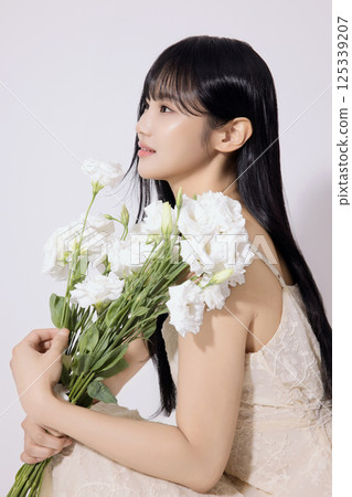 Portrait of a young woman sitting wearing a white dress and holding a bouquet of white flowers Portrait of a young woman sitting wearing a white dress and holding a bouquet of white flowers 125339207