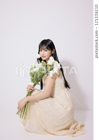 Portrait of a young woman sitting wearing a white dress and holding a bouquet of white flowers Portrait of a young woman sitting wearing a white dress and holding a bouquet of white flowers 125339210