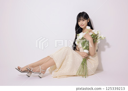 Portrait of a young woman sitting wearing a white dress and holding a bouquet of white flowers 125339213
