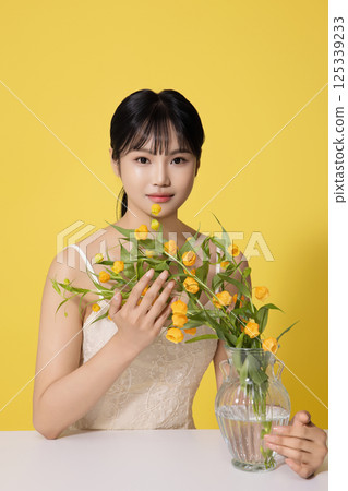 Portrait of a young woman sitting in front of a table with a vase of flowers 125339233