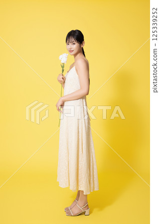 Portrait of young woman standing wearing white dress and holding white flowers 125339252