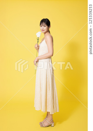 Portrait of young woman standing wearing white dress and holding white flowers 125339253