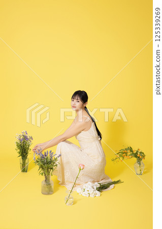 Portrait of a young woman sitting surrounded by glass bottles filled with flowers Portrait of a young woman sitting surrounded by glass bottles filled with flowers 125339269