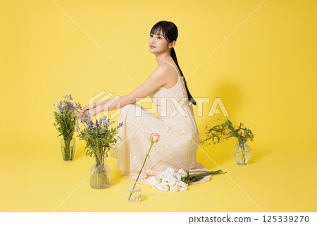 Portrait of a young woman sitting surrounded by glass bottles filled with flowers Portrait of a young woman sitting surrounded by glass bottles filled with flowers 125339270