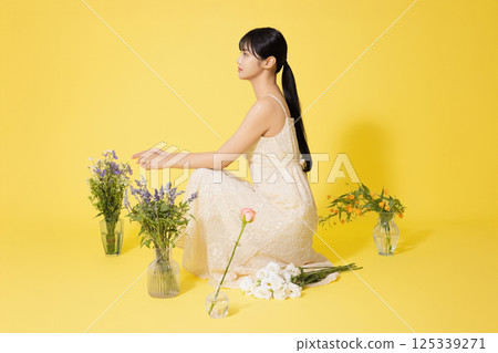 Portrait of a young woman sitting surrounded by glass bottles filled with flowers 125339271