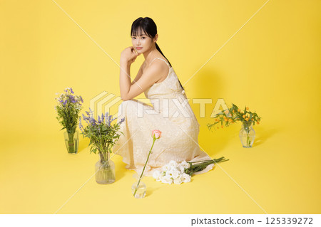 Portrait of a young woman sitting surrounded by glass bottles filled with flowers Portrait of a young woman sitting surrounded by glass bottles filled with flowers 125339272