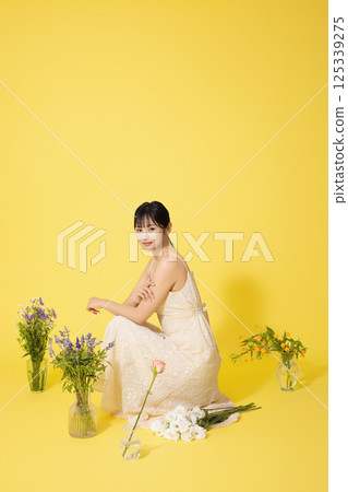 Portrait of a young woman sitting surrounded by glass bottles filled with flowers 125339275