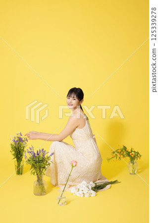 Portrait of a young woman sitting surrounded by glass bottles filled with flowers 125339278