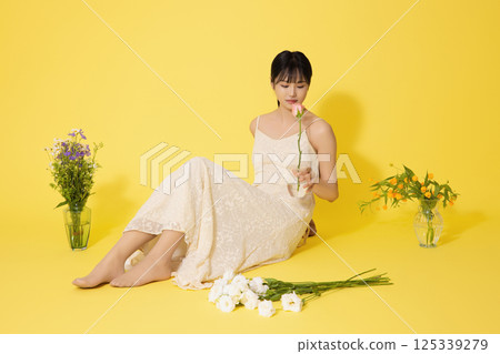 Portrait of a young woman sitting surrounded by glass bottles filled with flowers 125339279