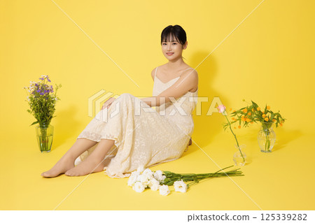 Portrait of a young woman sitting surrounded by glass bottles filled with flowers 125339282
