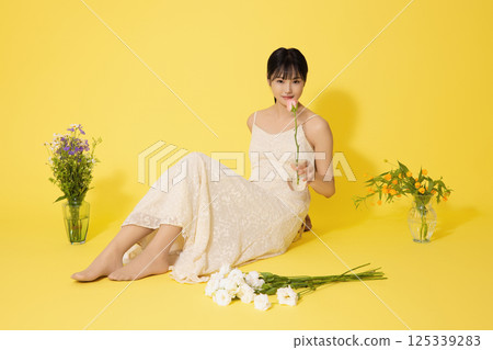 Portrait of a young woman sitting surrounded by glass bottles filled with flowers 125339283