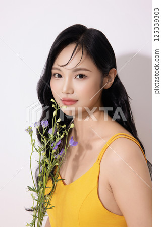 Portrait of young woman wearing yellow dress and holding bouquet of flowers Portrait of young woman wearing yellow dress and holding bouquet of flowers 125339303