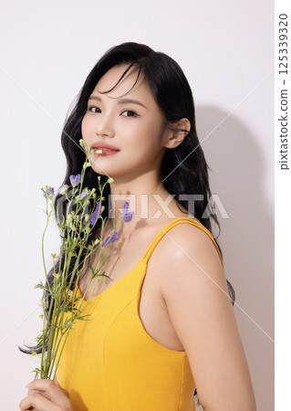 Portrait of young woman wearing yellow dress and holding bouquet of flowers 125339320