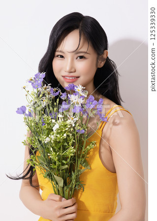 Portrait of young woman wearing yellow dress and holding bouquet of flowers 125339330