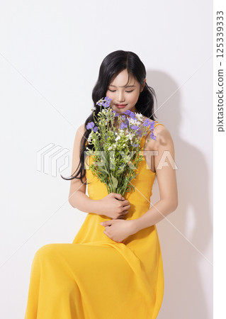Portrait of young woman wearing yellow dress and holding bouquet of flowers 125339333