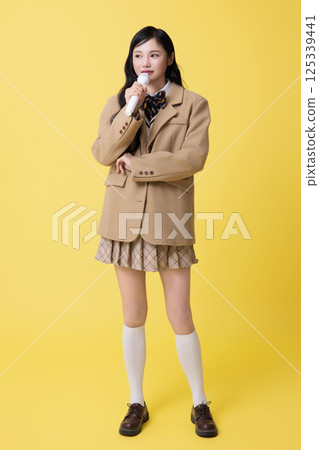 A girl wearing a school uniform and singing with a microphone A girl wearing a school uniform and singing with a microphone 125339441
