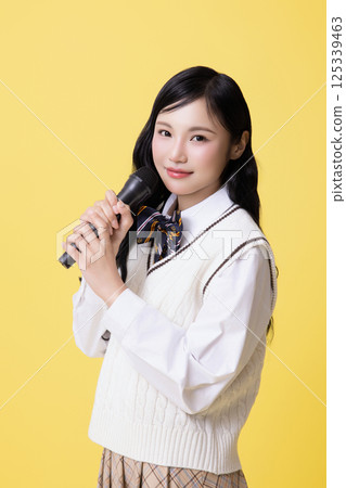 A girl wearing a school uniform and singing with a microphone A girl wearing a school uniform and singing with a microphone 125339463