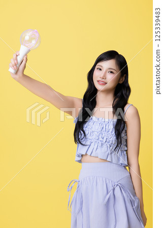 A girl wearing a stage costume and posing with a light stick 125339483