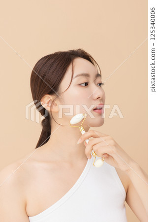 Portrait of a young woman massaging her skin using gua sha 125340006