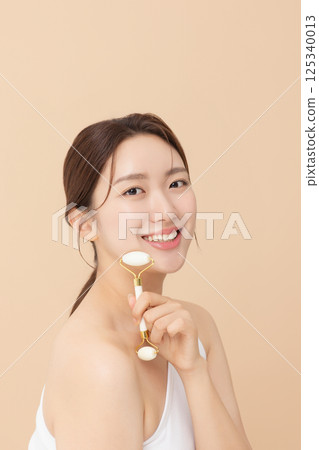 Portrait of a young woman massaging her skin using gua sha 125340013