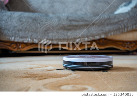 Robot vacuum autonomously cleaning a carpet at home. Concept of smart cleaning technology and automated home maintenance. Robot vacuum autonomously cleaning a carpet at home. Concept of smart cleaning technology and automated home maintenance. 125340033