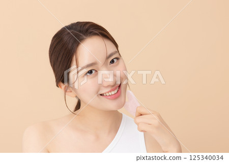 Portrait of a young woman massaging her skin using gua sha Portrait of a young woman massaging her skin using gua sha 125340034